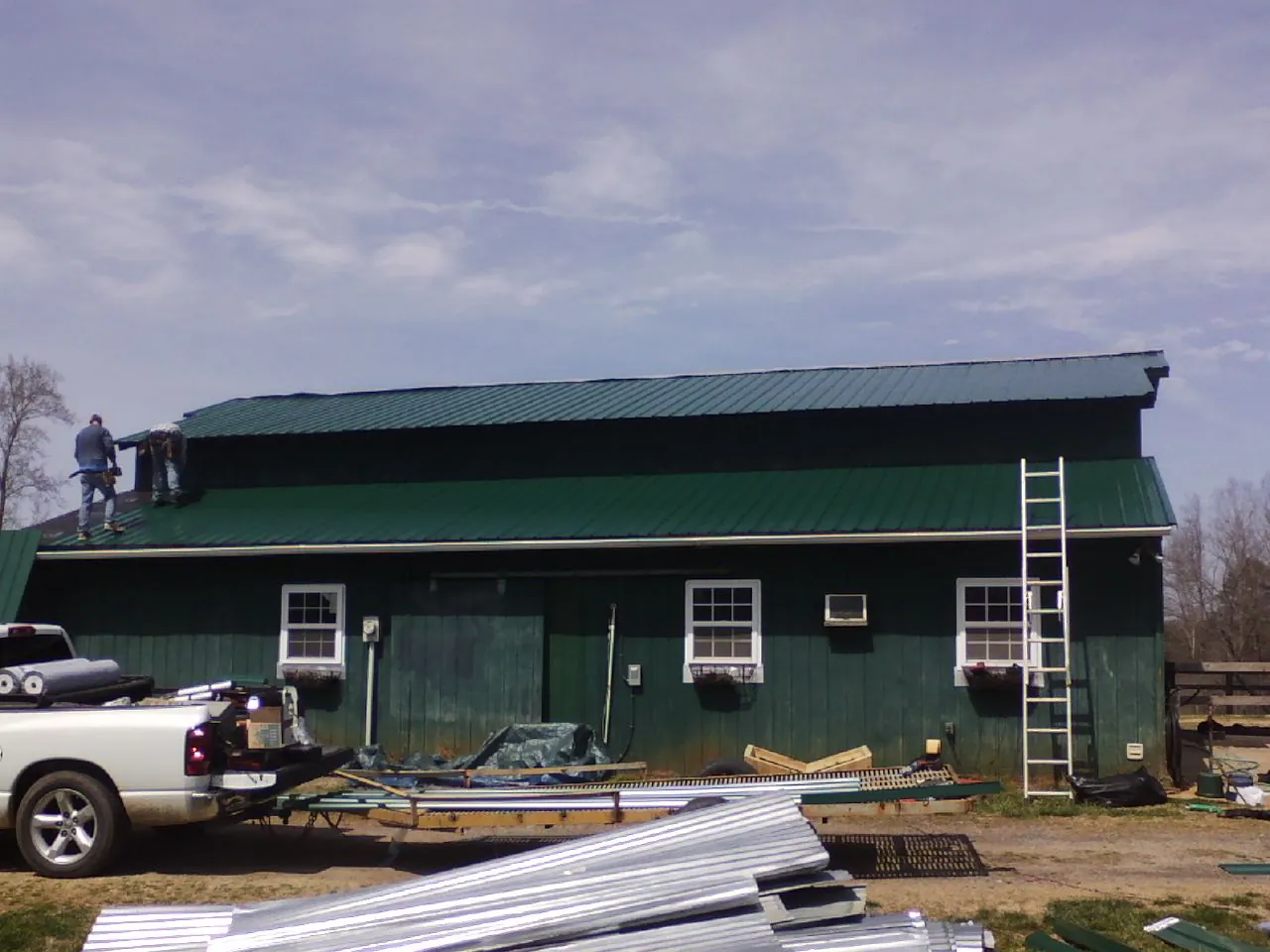 Crew installing green metal roofing on a large green barn in Southampton